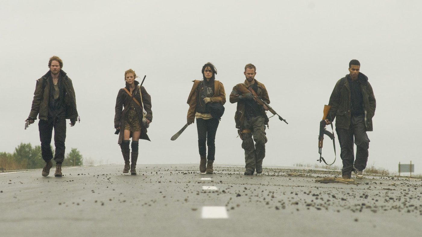 Five survivors walking down an empty highway under flat grey sky in The Day: Shawn Ashmore, Ashley Bell, Shannyn Sossamon, Dominic Monaghan and Cory Hardrict.